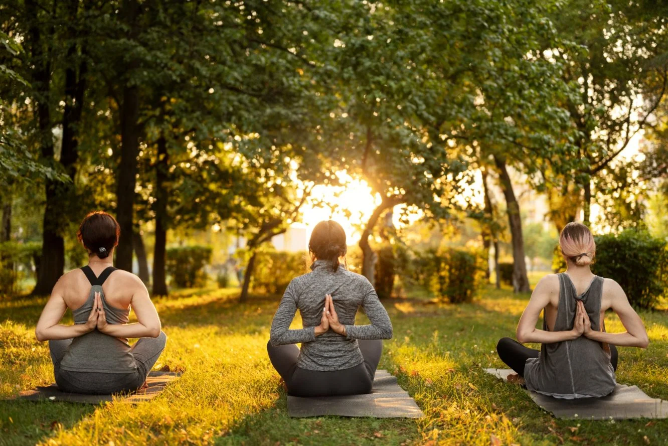 Back view of women meditating outdoors, practicing stress management techniques for busy lives.